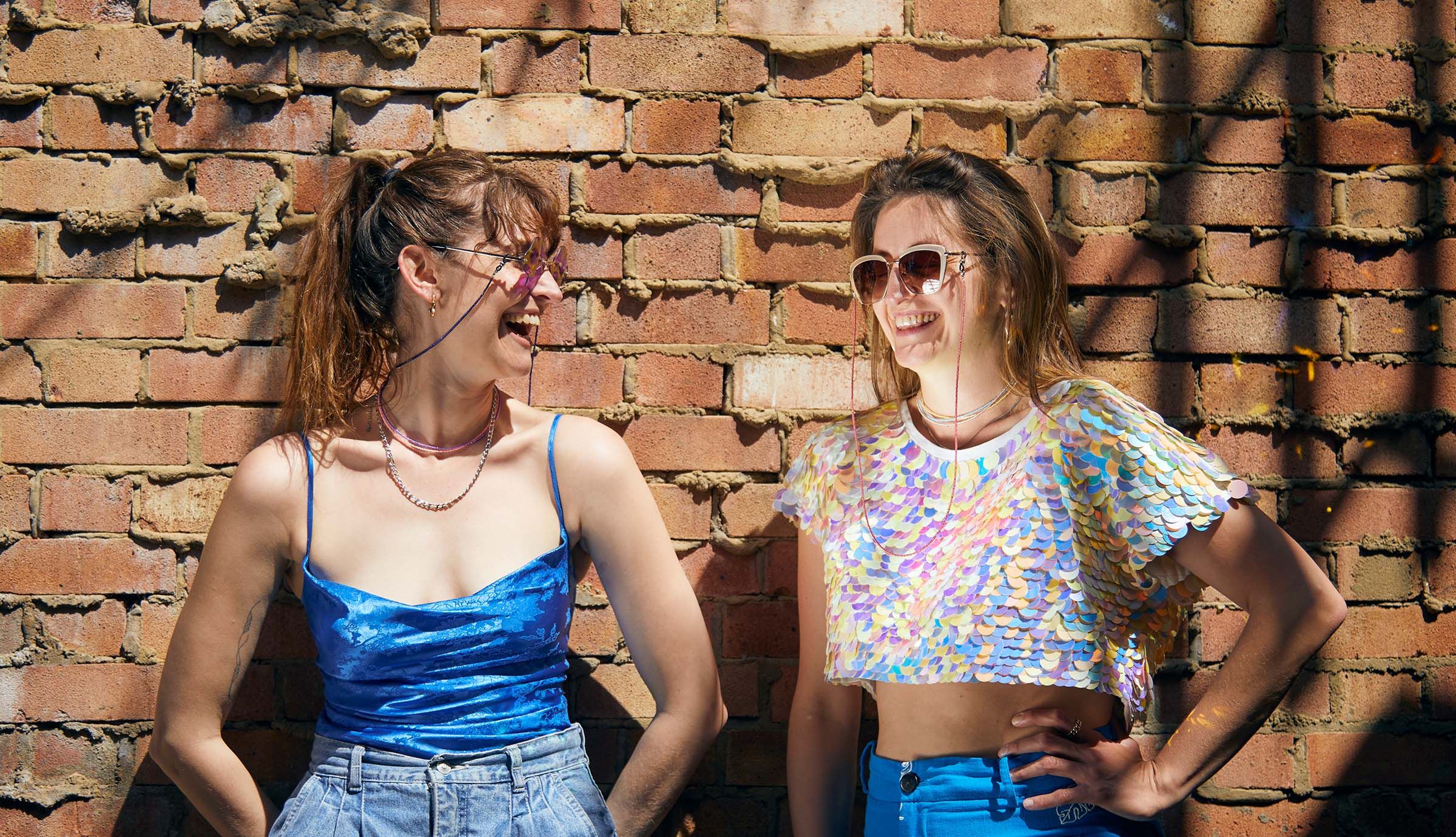 Models are wearing silver figaro chain, luna flamingo, purple orchid, ocean blue, and sun glow  bead necklaces; with navy and light cranberry celeste bead glasses chain